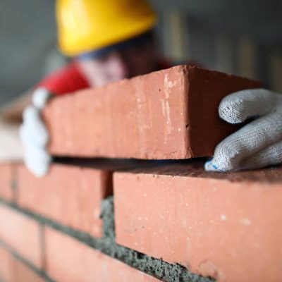 Close-up of professional construction worker laying bricks in industrial site. Builder in protective uniform. Man building wall with blocks. Renovation concept